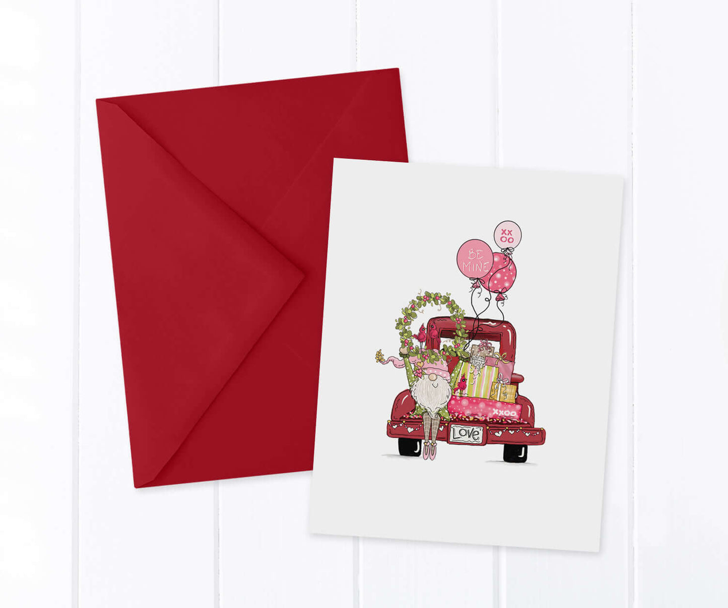 Valentine Gnome holding a wreath over his head in front of a vintage red pickup truck filled with presents